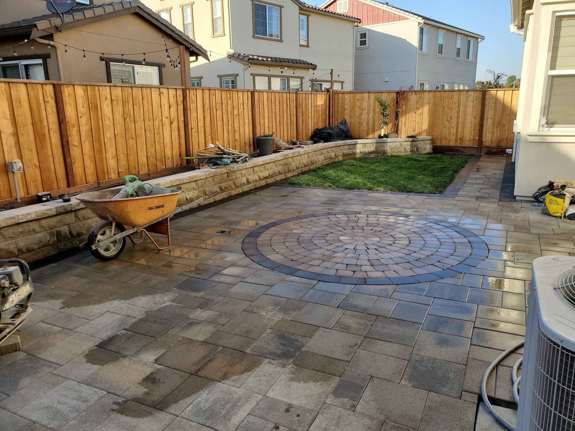 Paver patio featuring a circular medallion inlay, a new retaining wall, and fresh sod