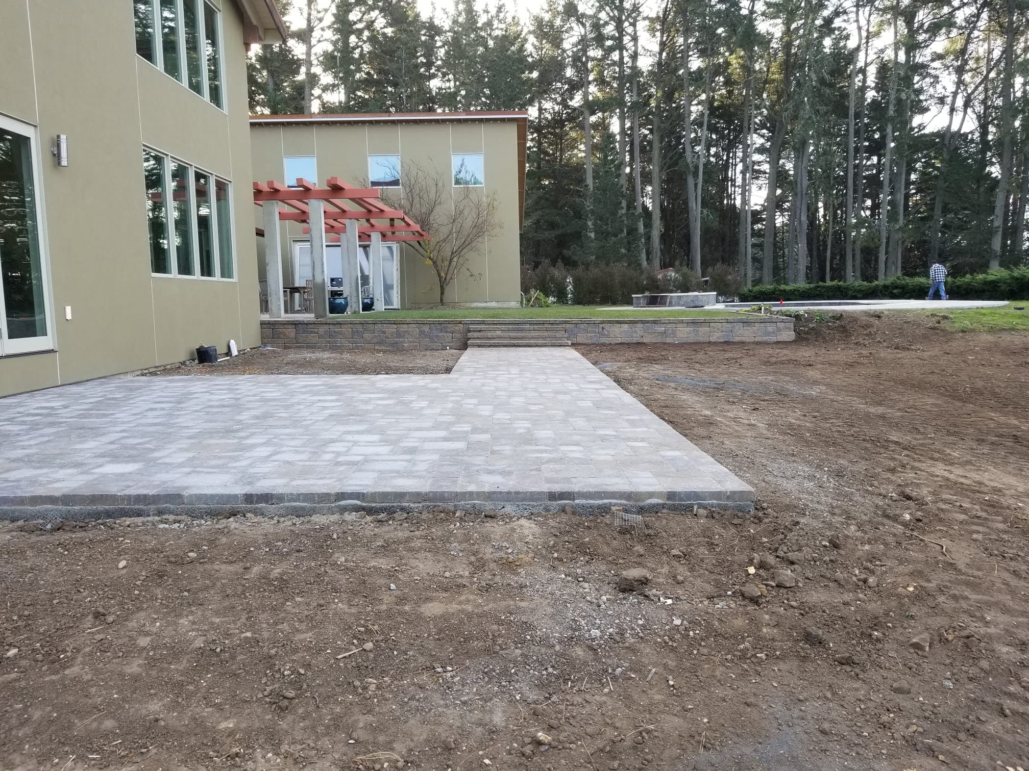 Paver patio and retaining wall installation behind a modern Bay Area home surrounded by pines